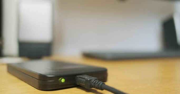 Blinking indicator light during external hard drive operation, data exchange, close-up. HDD lies on desktop, indication of work.
