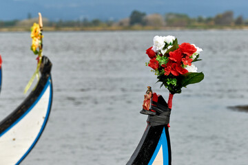 statue of the Virgin surrounded by flowers on the bow of colorful typical boats in the harbor of...