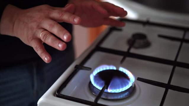A man warms his hands over a burning fire. Natural gas burns on a stove