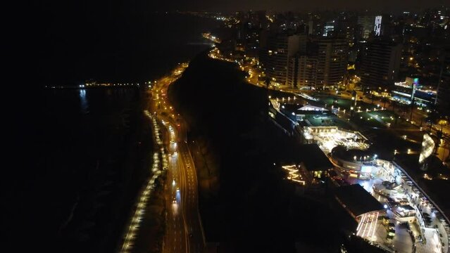Drone timelapse video of night time Miraflores district of Lima, Peru. To left coastal freeway cars and right shopping center Larcomar. Shot flying forward tilting camera up.