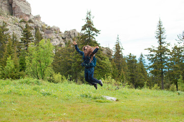 young female traveler with a backpack looks at the mountains. Hiking is an active lifestyle of...