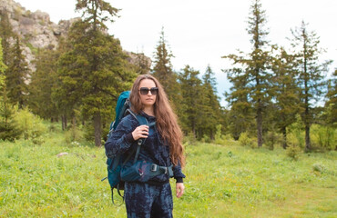 young female traveler with a backpack looks at the mountains. Hiking is an active lifestyle of...