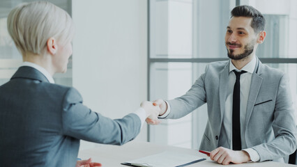HR male manager shaking hand to female candidate after having job interview in modern office indoors