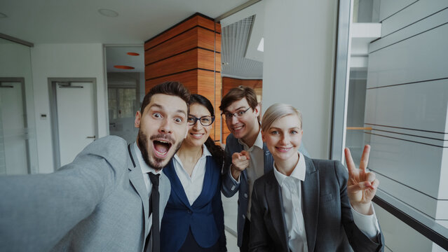 POV of Happy business team taking selfie portrait on smartphone camera and posing for group photo during meeting in modern office indoors