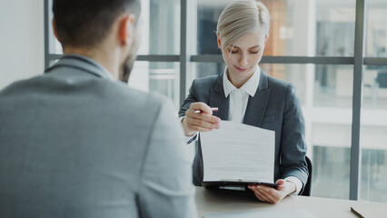 HR businesswoman having job interview with young man in suit and watching his resume application in modern office indoors