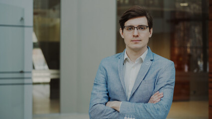 Portrait of successful smiling businessman in glasses looking into camera in modern office indoors