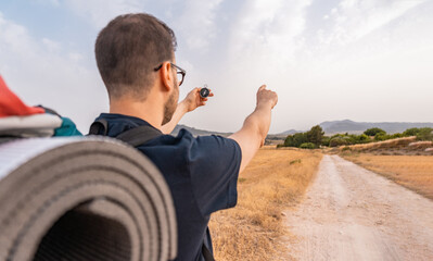 Viajero irreconocible señalando la direccion del camino, con un brújula, en un camino entre...