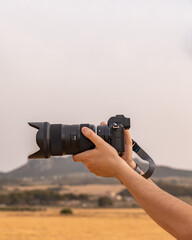 Detalle de mano cogiendo unas cámara de fotografía, en un bonito paisaje. Fotografía horizontal,...