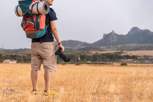 Hombre con mochila de acampada y esterilla, con su c&aacute;mara de fotograf&iacute;a, en un paisaje de prados y monta&ntilde;as. Fotograf&iacute;a horizontal con espacio para texto.