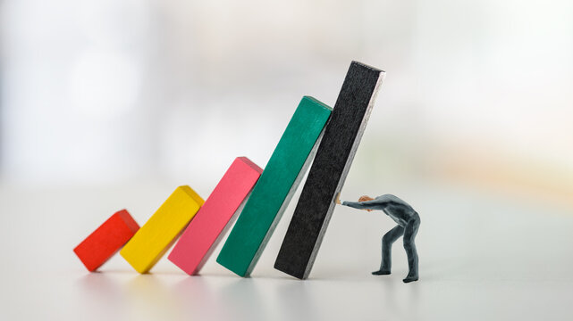Company domino effect or chain reaction, financial concept : Businessman CEO pushes wood bar graphs to prevent or keep them from collapsing, depicting stopping problems or crisis from contagion effect