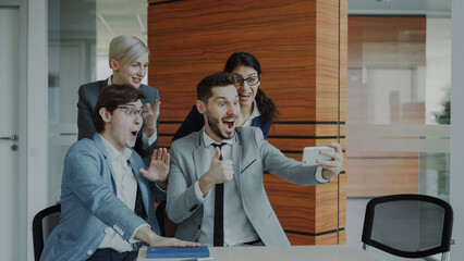 Fototapeta premium Happy business team taking selfie portrait on smartphone camera and posing for group photo during meeting in modern office indoors