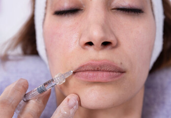 Cosmetologist performs lip filler injections with hyaluronic acid filler in a woman's face...