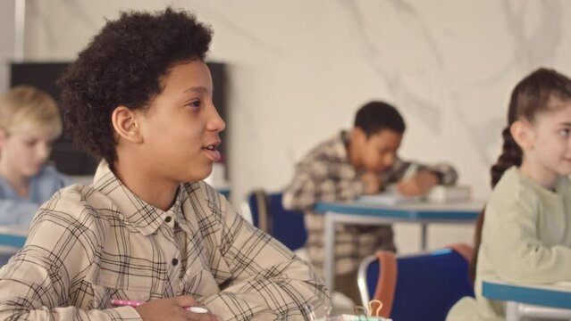 Chest up slowmo of African American middle school girl raising hand and asking teacher question during lesson in modern classroom