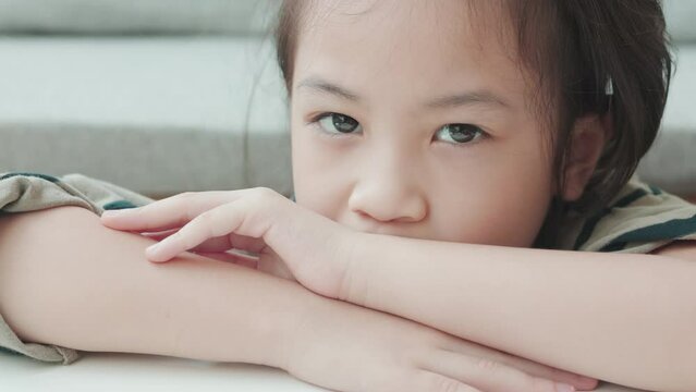 Face close up of adorable asian girl in comfortable living room at home looks at the camera with smiling and shows positive emotion, enjoyment, happiness of child with beautiful sunlight.
