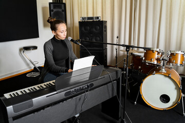 Young Asian or Caucasian brunette woman singing song on mic and playing digital keyboard electronic...
