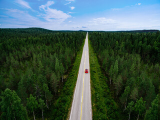 Aerial view of red car wdriving the route through green summer woods in Finland.