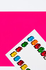 Flat lay of colorful gummy bears on white and pink background.