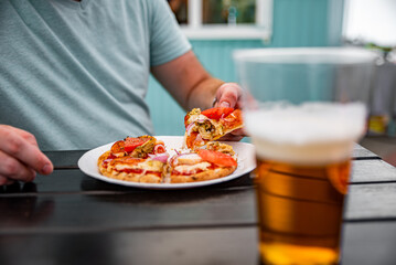 man Hand takes a slice of pita Pizza with Mozzarella cheese, ham, bacon, tomato, Spices in outdoor cafe