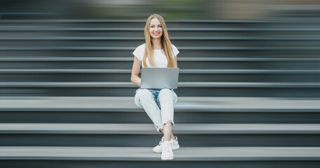 Young student girl sitting with laptop on stairs near university smiling working and look camera