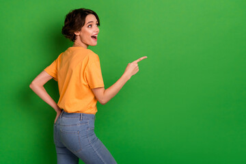 Photo of cute excited young woman dressed orange t-shirt looking pointing empty space isolated green color background