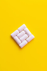 Flat lay of chewing gums in square shape on yellow background.