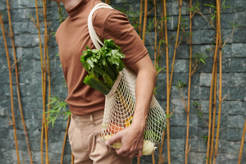 Young man holding mesh bag of fresh groceries he bought at local market