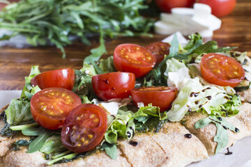 Homemade pinsa with cheese, tomatoes, cabbage and arugula close-up sharpness in the foreground.