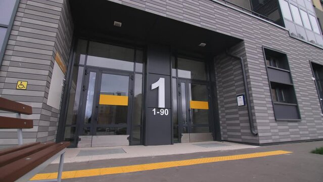 Stylish glass entrance to contemporary multistory residential building with porch and apartments numbers in city