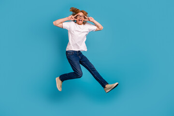 Obraz premium Full body photo of carefree crazy man jumping demonstrate v-sign near eyes isolated on blue color background