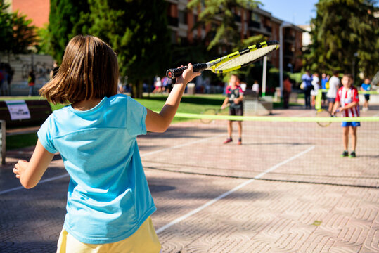 Niña sin identificar, de espaladas, jugando al tenis, golpeando la pelota con la raqueta de color amarilla, en el parque de la ciudad o del pueblo., deporte