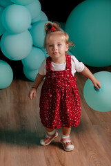 Child in a red dress celebrates his birthday against the backdrop of huge balloons. Child's holiday.