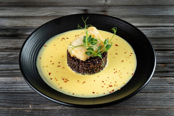 Risotto with slice roasted white fish, cod on black background. Grilled code with mix brown and wild rice in dark style.