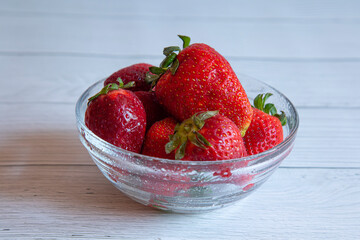 strawberries in a transparent bowl on a white wooden table
