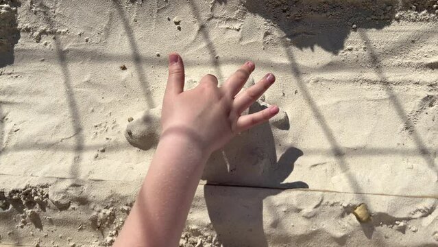 a child sculpts a turtle figurine out of sand, draws with a finger, hands close-up, slow motion. The shadow of a volleyball net on the sand. The concept of children's beach sports