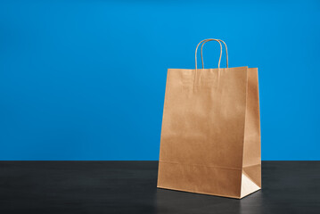 A brown paper bag with handles on a blue background. ECO bag. Craft paper bag. Recycled paper....
