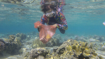 Woman in diving equipment swims and collects plastic debris underwater on the bottom of coral reef....