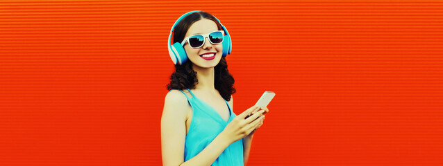Portrait of happy smiling young woman in headphones listening to music with smartphone on red background, blank copy space for advertising text
