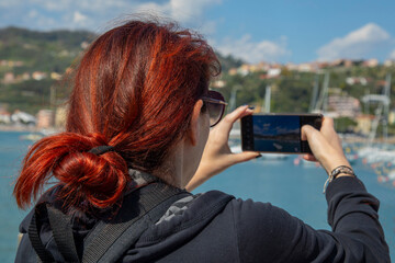woman with red hair takes a picture of a seaport on her phone