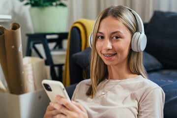 portrait of teenager girl with teeth brace listening music on headphones and looking at camera