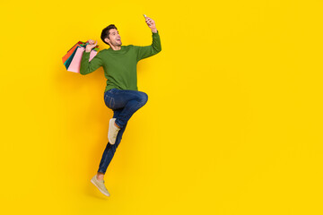 Photo of funky funny guy dressed green pullover jumping holding bags portrait device empty space isolated yellow color background