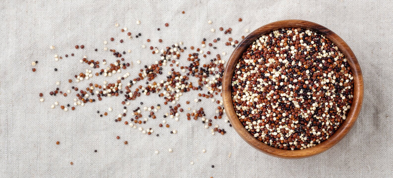 Red, black and white quinoa in wooden bowl on linen cloth background