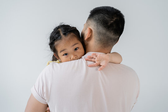 back view of father with beard holding in arms asian daughter isolated on grey.