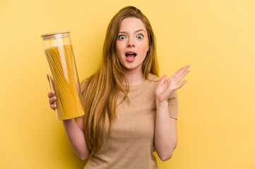 Young caucasian woman holding a spaghettis jar isolated on yellow background surprised and shocked.