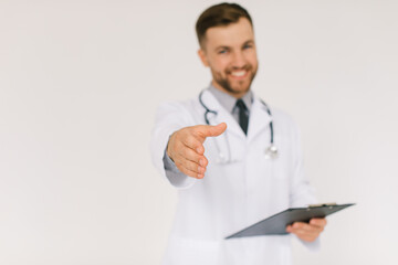 The happy doctor with a stethoscope and a folder extends a hand of greetings on a white background