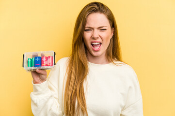 Young caucasian woman holding a battery box isolated on yellow background screaming very angry and aggressive.