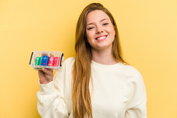 Young caucasian woman holding a battery box isolated on yellow background happy, smiling and cheerful.