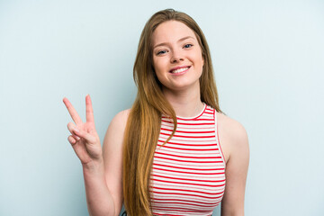 Young caucasian woman isolated on blue background showing victory sign and smiling broadly.