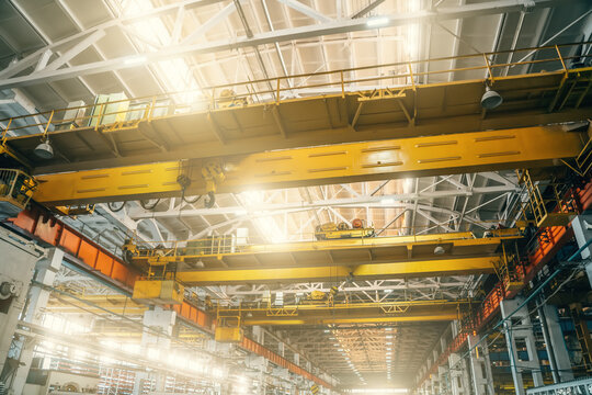 Yellow overhead or beam or bridge cranes in industrial metalworking factory.