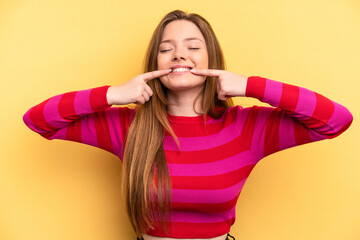 Young caucasian woman isolated on yellow background smiles, pointing fingers at mouth.