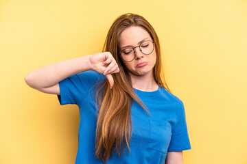 Young caucasian woman isolated on yellow background showing a dislike gesture, thumbs down....